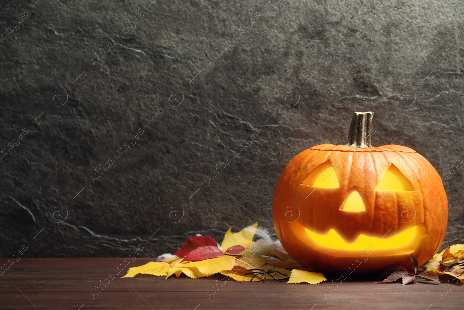 Photo of Pumpkin jack o'lantern and autumn leaves on wooden table, space for text. Halloween decor