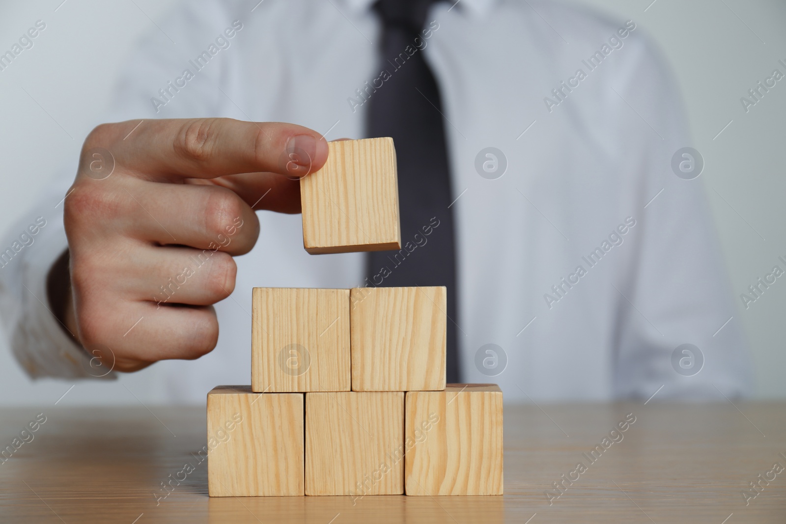 Photo of Businessman building pyramid of blank cubes on wooden table, closeup. Space for text