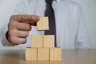 Photo of Businessman building pyramid of blank cubes on wooden table, closeup. Space for text