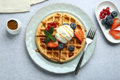 Delicious Belgian waffles with ice cream, berries and caramel sauce served on grey table, flat lay