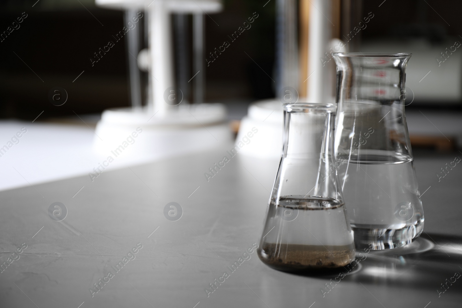 Photo of Glassware with soil extract and water on grey table, space for text. Laboratory research