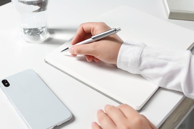 Woman writing in notebook at white table, closeup