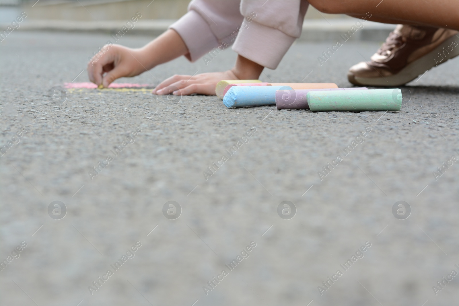 Photo of Little child drawing butterfly and hearts with chalk on asphalt, closeup. Space for text