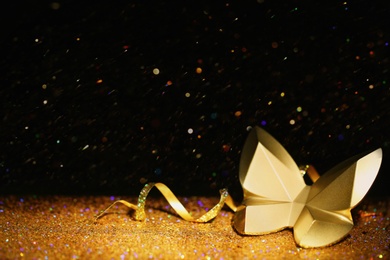 Photo of Golden glitter, decorative butterfly and streamer against black background. Space for text