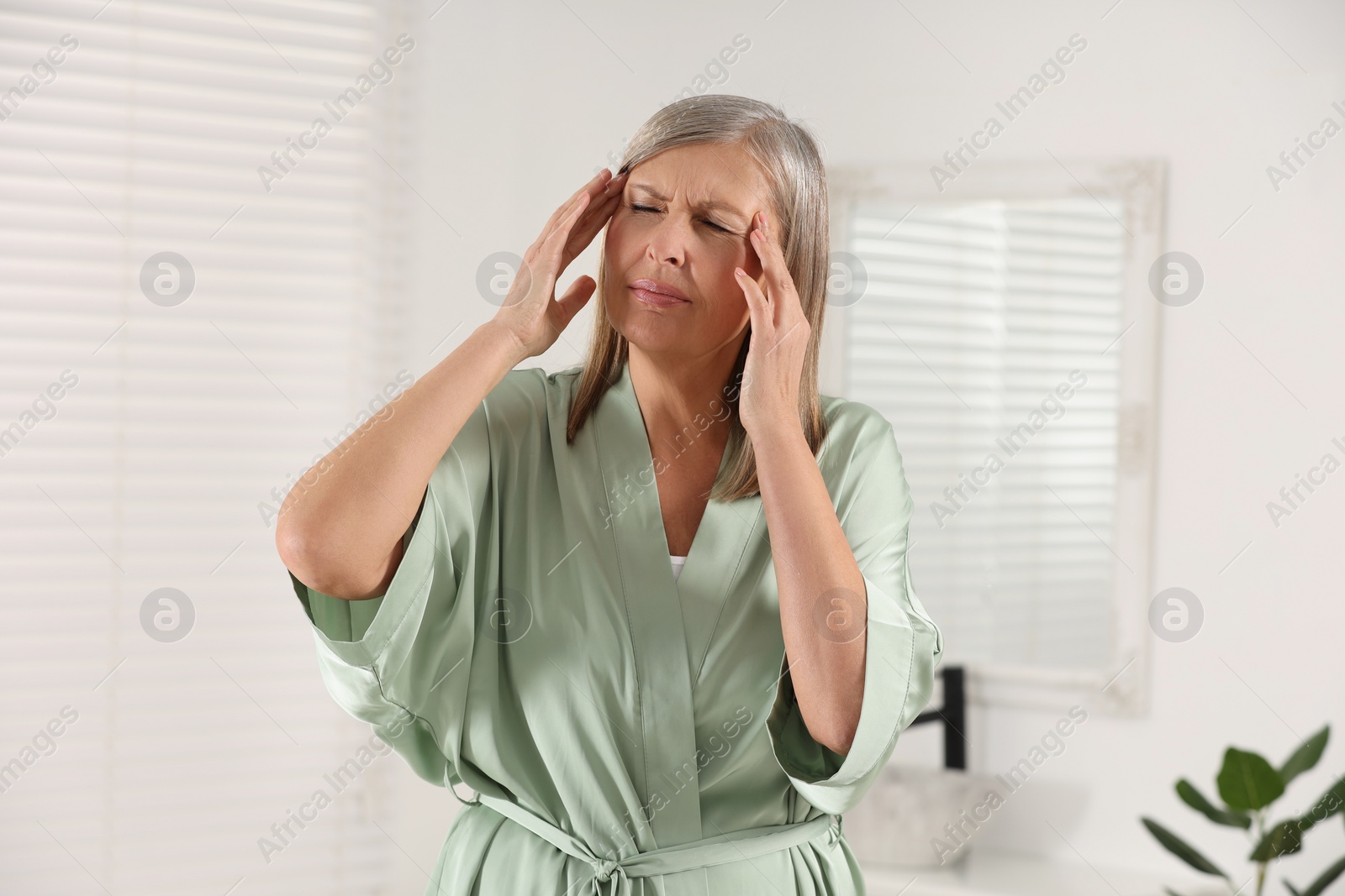 Photo of Menopause. Woman suffering from headache in bathroom