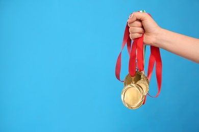 Woman holding gold medals on light blue background, closeup. Space for text