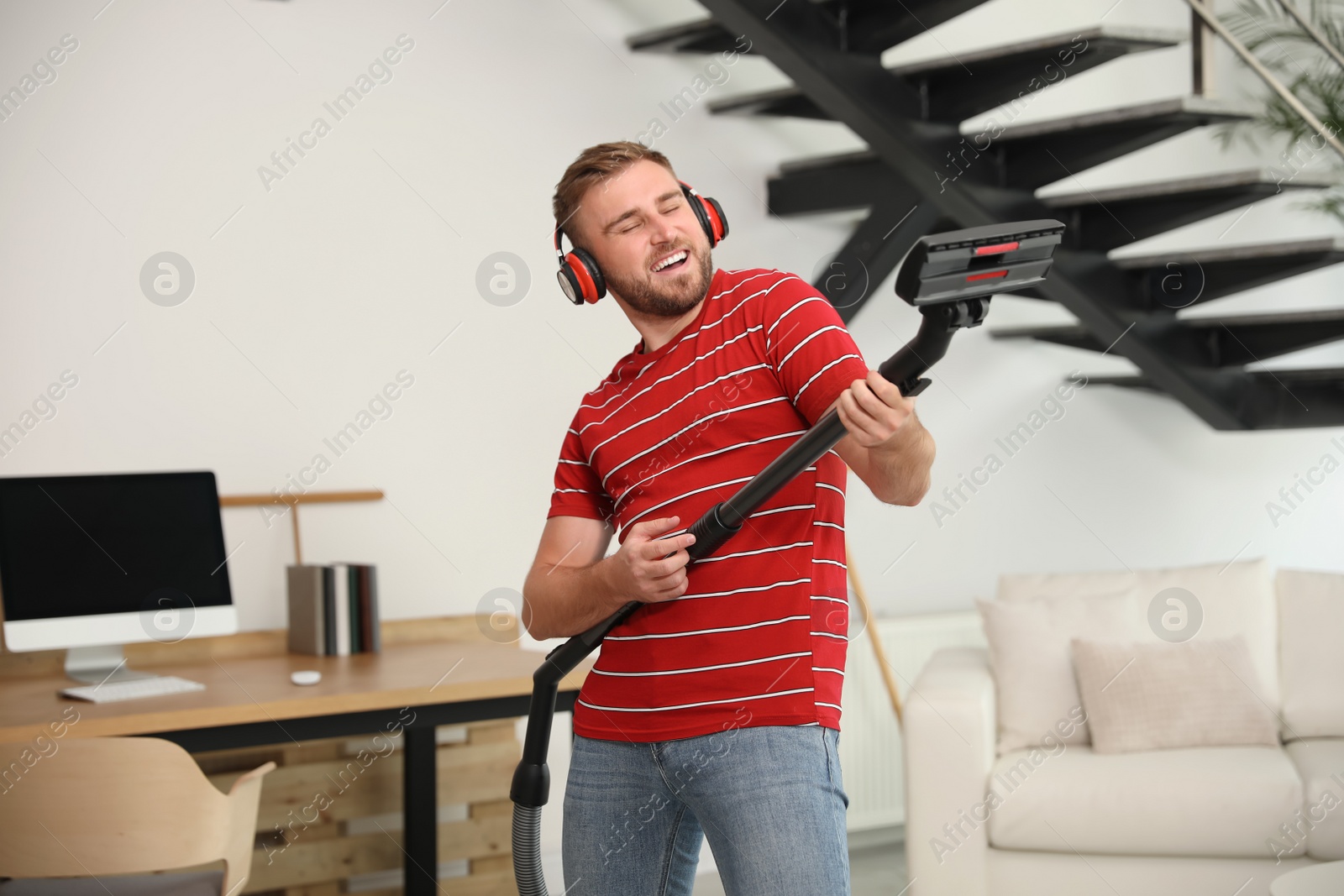 Photo of Young man having fun while vacuuming in living room