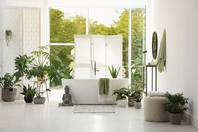 Photo of Stylish bathroom interior with modern tub, window and beautiful houseplants. Home design