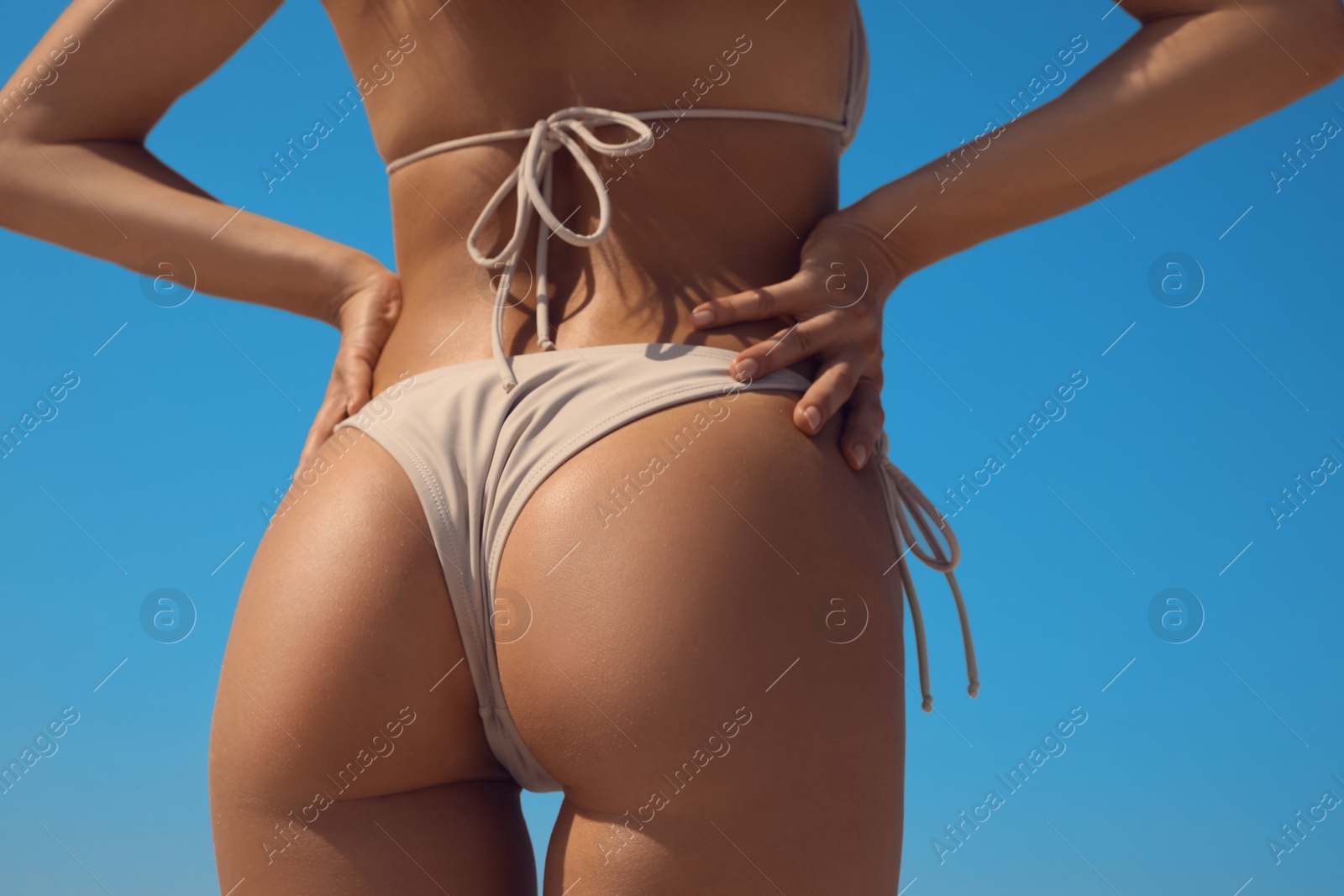 Photo of Woman with perfect body in bikini against blue sky, closeup. Back view