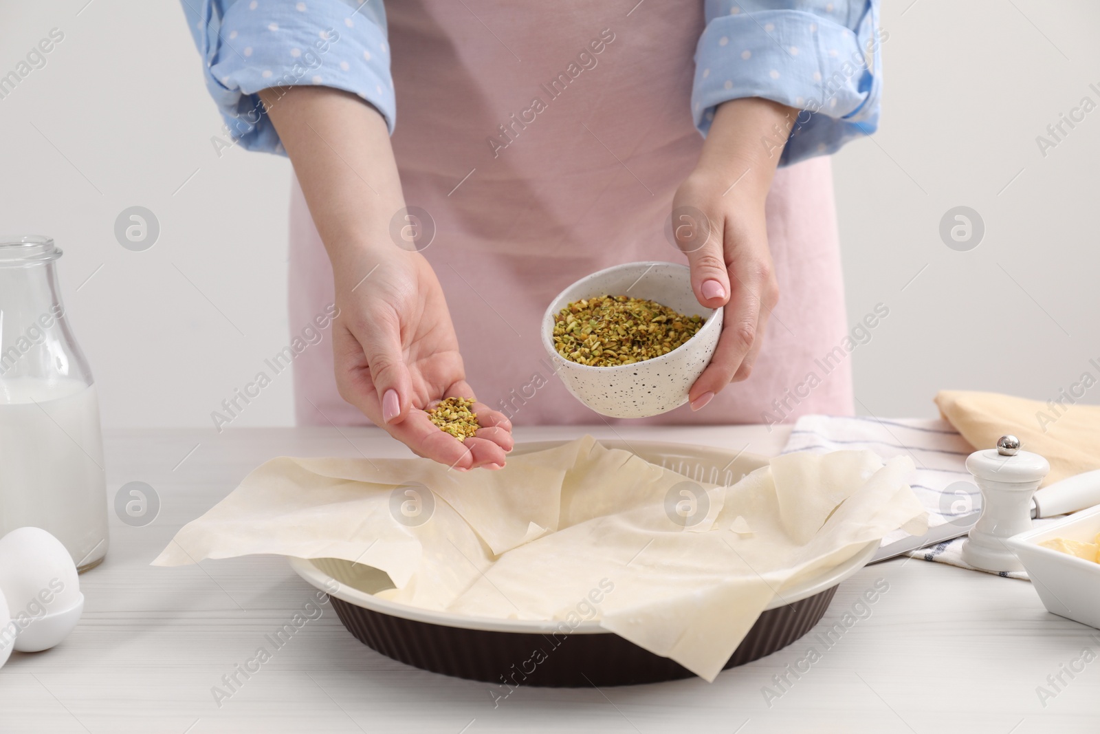 Photo of Woman putting filling into baking dish with dough to prepare baklava at white wooden table, closeup