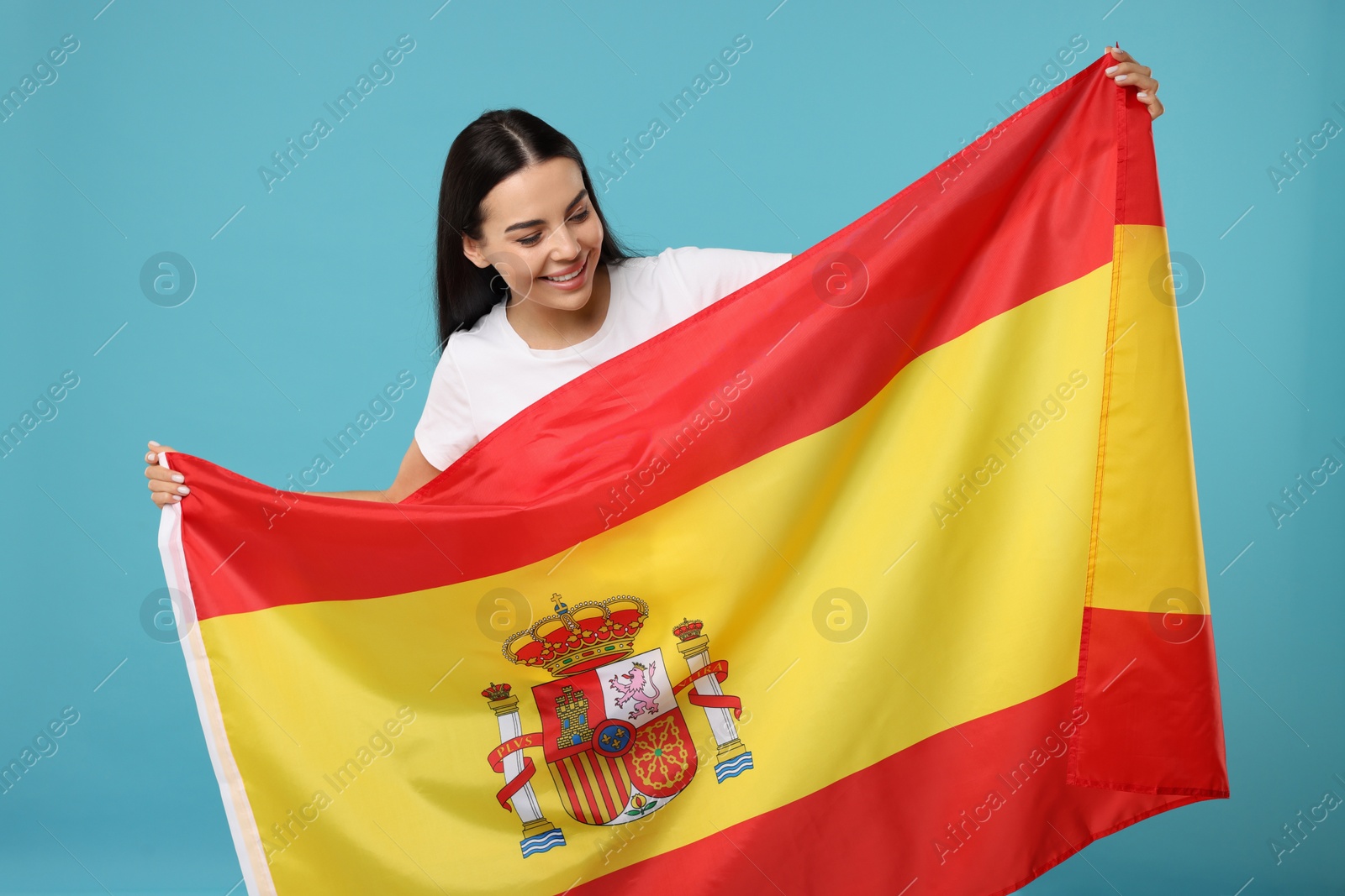 Photo of Happy young woman with flag of Spain on light blue background