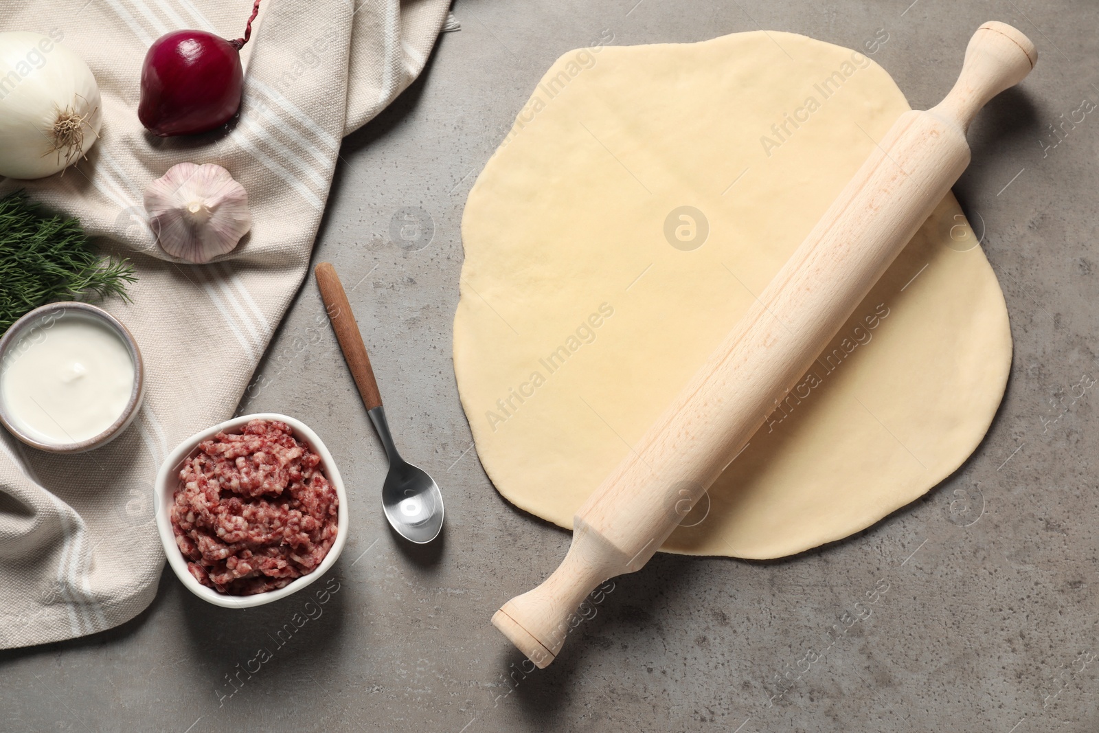 Photo of Raw dough, rolling pin and products on grey table, flat lay