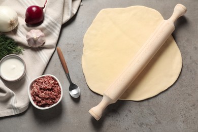 Raw dough, rolling pin and products on grey table, flat lay