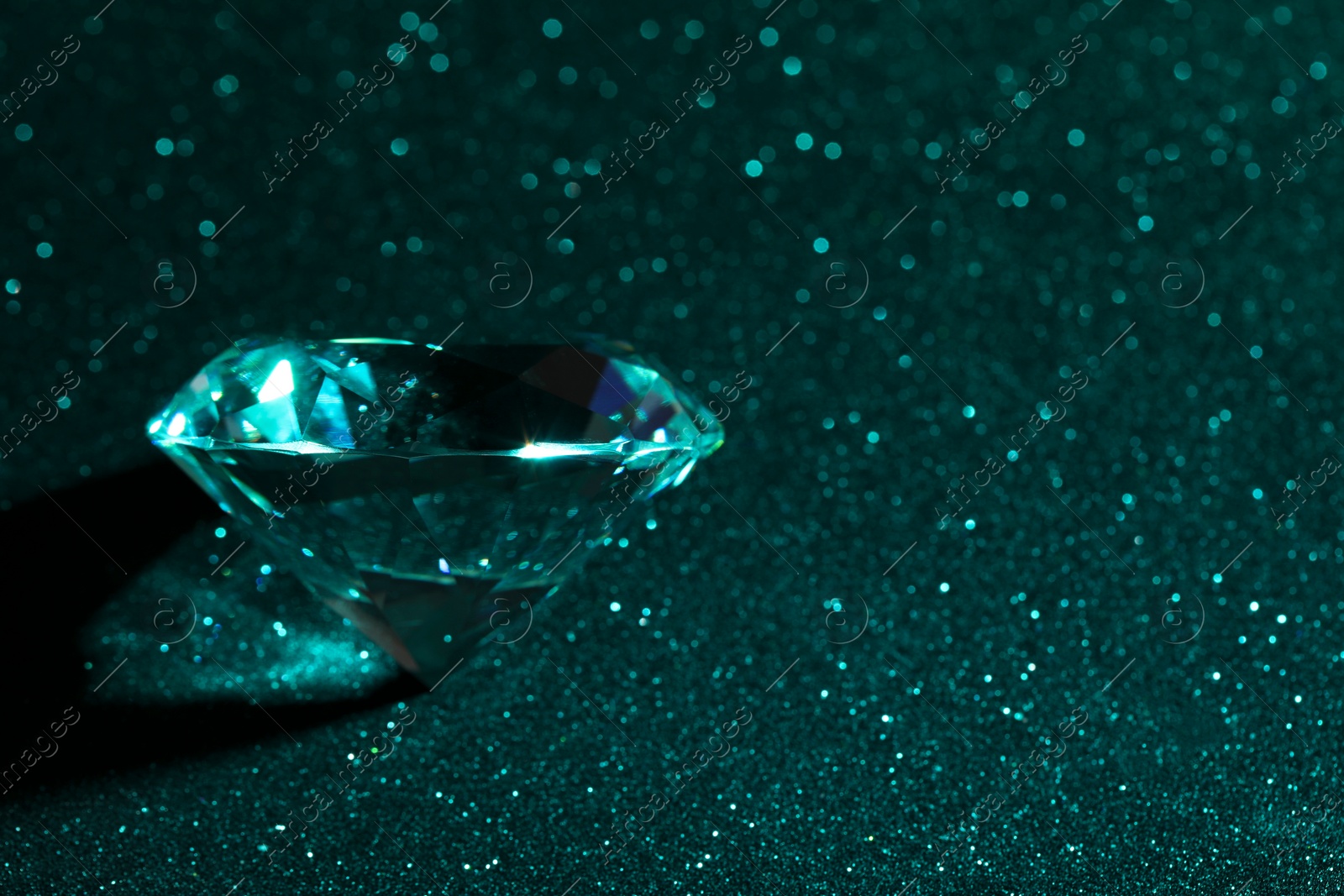 Photo of Beautiful dazzling diamond on green glitter surface, closeup. Space for text