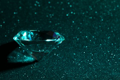 Photo of Beautiful dazzling diamond on green glitter surface, closeup. Space for text