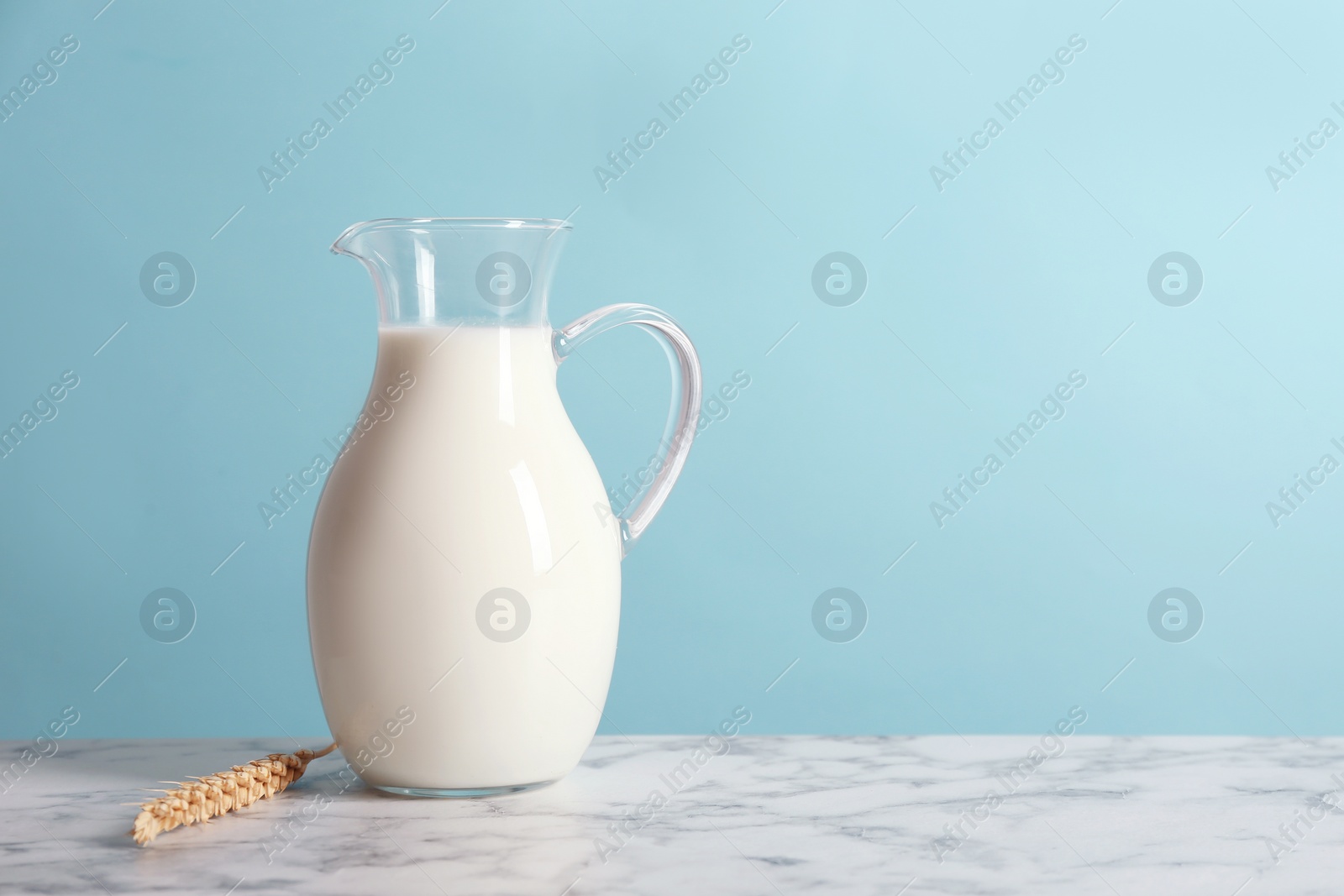 Photo of Jug with milk on table against color wall