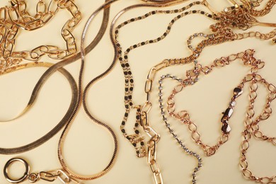 Photo of Different metal chains on beige background, above view. Luxury jewelry