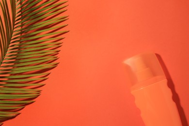 Photo of Sunscreen and tropical leaf on coral background, flat lay and space for text. Sun protection care