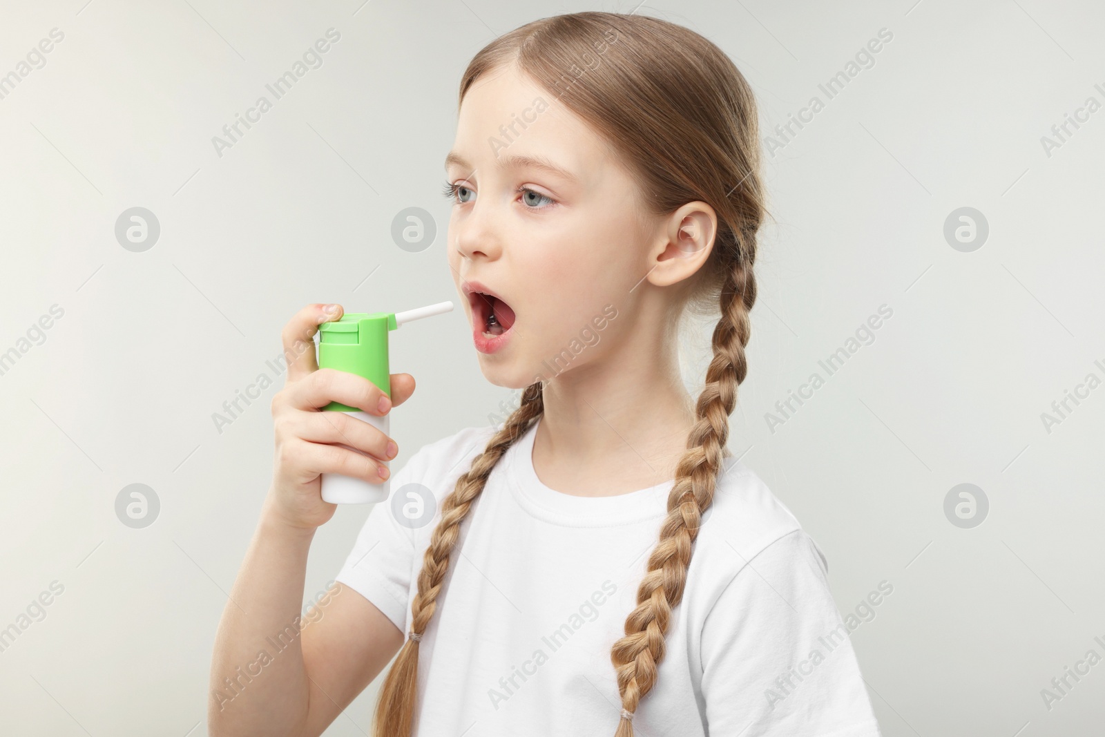 Photo of Little girl using throat spray on light grey background