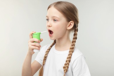 Little girl using throat spray on light grey background