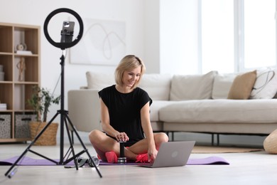 Smiling sports blogger streaming online fitness lesson with smartphone at home