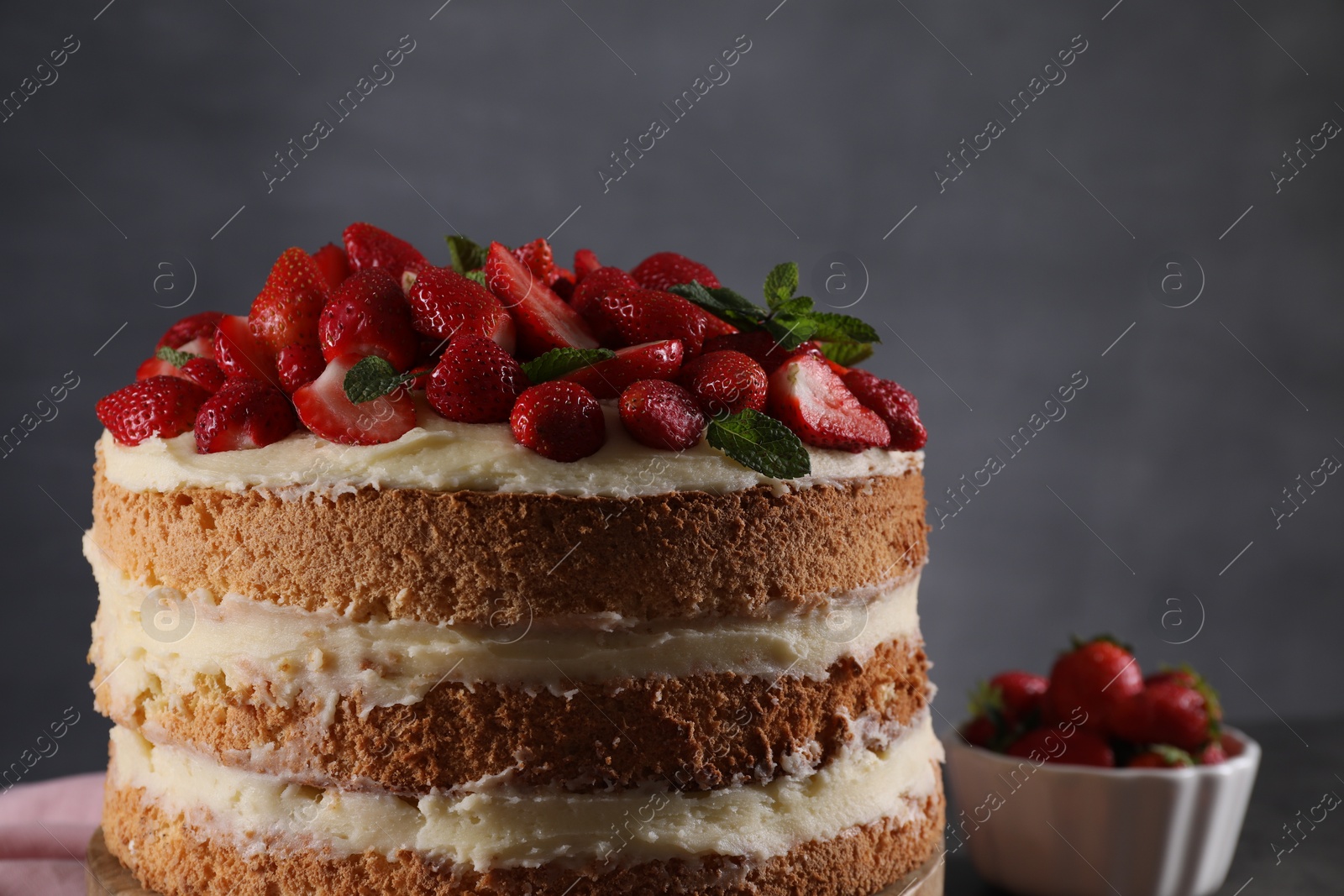 Photo of Tasty cake with fresh strawberries and mint against dark gray background