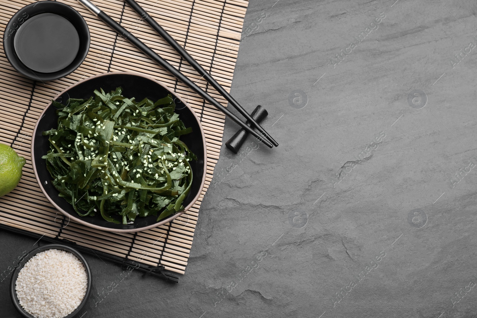 Photo of Fresh laminaria (kelp) seaweed served on black table, flat lay. Space for text