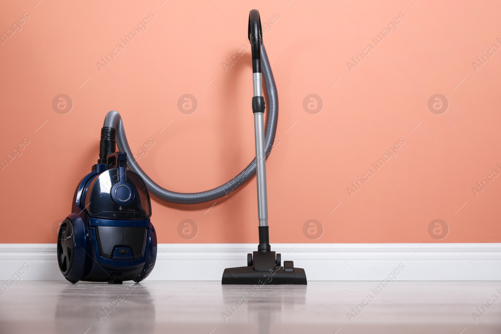 Photo of Modern vacuum cleaner on floor near orange wall indoors. Space for text