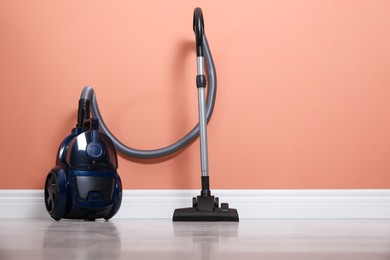 Photo of Modern vacuum cleaner on floor near orange wall indoors. Space for text