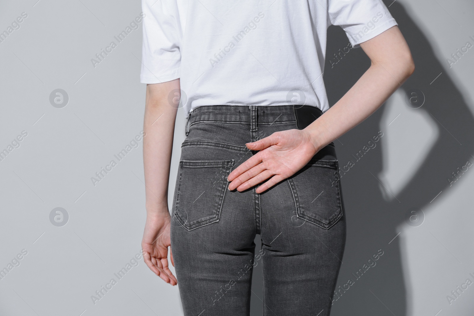 Photo of Woman showing open palm behind her back on light background, back view