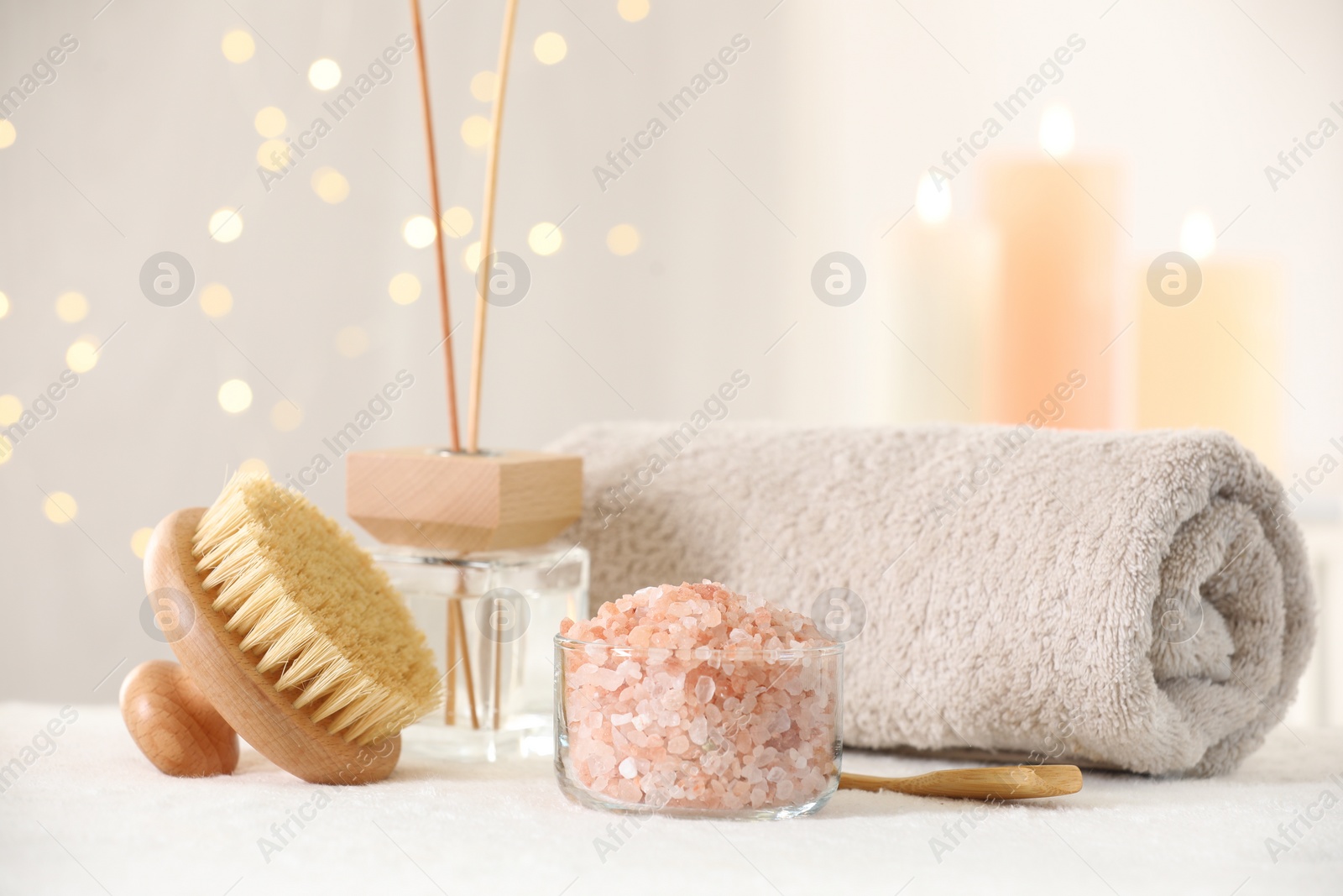 Photo of Spa composition. Sea salt, brush, towel and reed air freshener on soft white surface