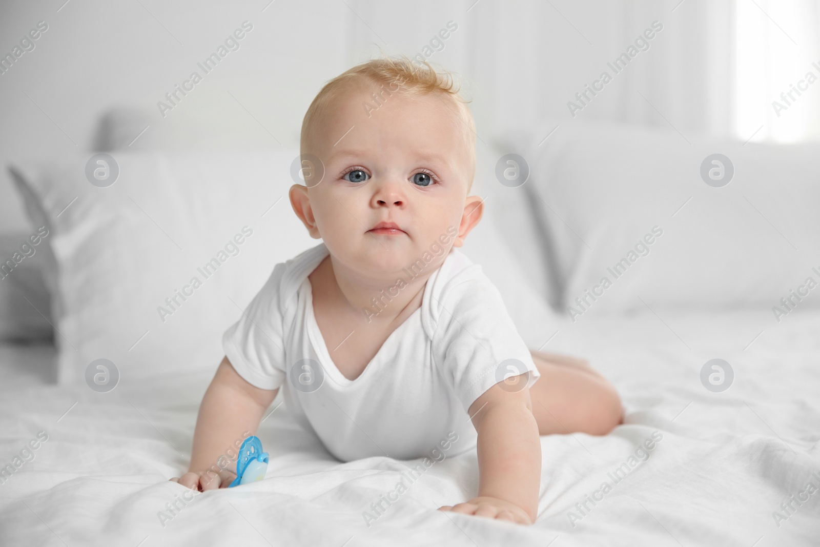 Photo of Cute baby with pacifier lying on bed at home