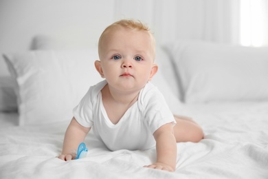 Cute baby with pacifier lying on bed at home