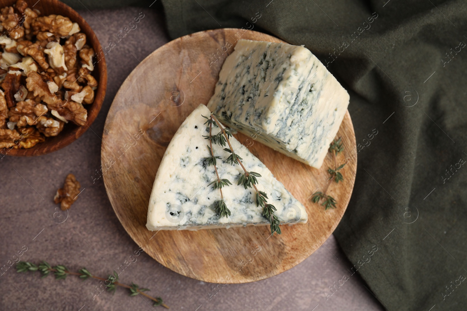 Photo of Tasty blue cheese with thyme and walnuts on brown table, flat lay