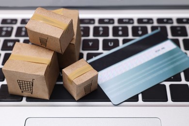 Image of Internet store. Small cardboard boxes with shopping carts, credit card on laptop, closeup