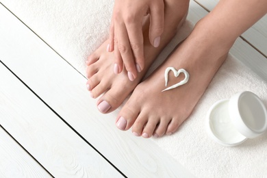 Photo of Woman applying foot cream on white wooden floor, closeup with space for text. Spa treatment
