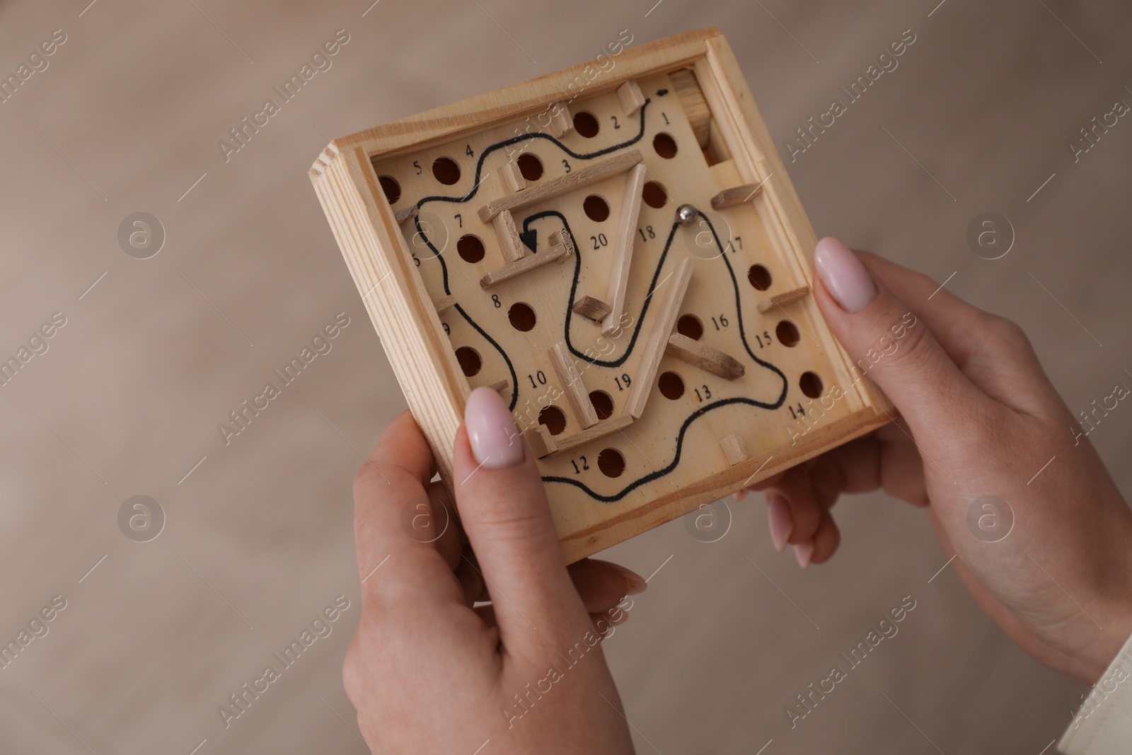 Photo of Woman holding wooden toy maze with metal ball on blurred background, closeup