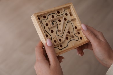 Photo of Woman holding wooden toy maze with metal ball on blurred background, closeup