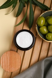 Jar of natural cream, olives and leaves on beige background, flat lay