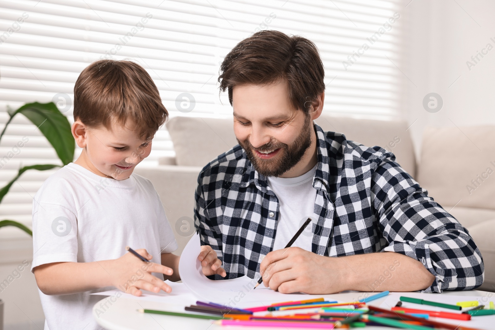 Photo of Happy dad and son drawing together at table indoors