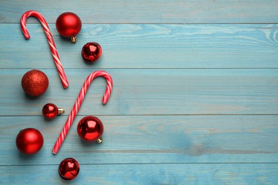 Tasty candy canes and Christmas balls on light blue wooden table, flat lay. Space for text