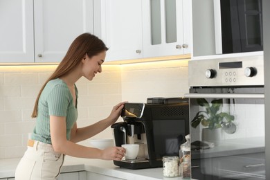 Photo of Young woman preparing fresh aromatic coffee with modern machine in kitchen