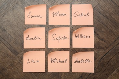 Photo of Paper stickers with different names on wooden background, flat lay. Choosing baby's name