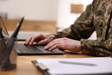 Photo of Military service. Soldier working with laptop at wooden table indoors, closeup