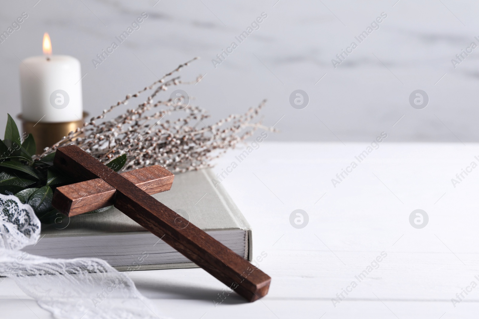 Photo of Burning candle, bouquet with willow branches, book and cross on white wooden table, space for text