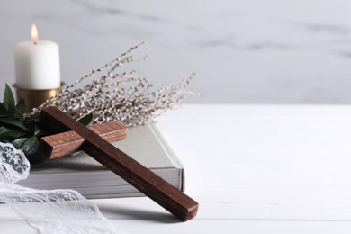 Photo of Burning candle, bouquet with willow branches, book and cross on white wooden table, space for text