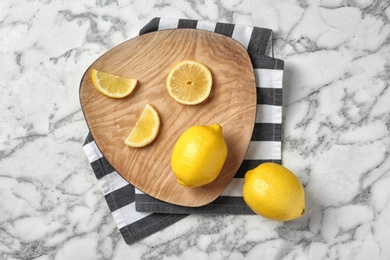 Wooden board with lemons on marble background, top view