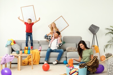 Photo of Frustrated mother trying to clean up mess while father playing with children in room