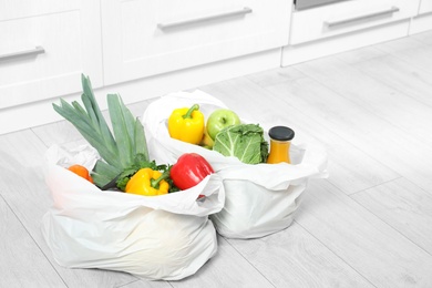 Plastic shopping bags full of vegetables and juice on floor in kitchen. Space for text