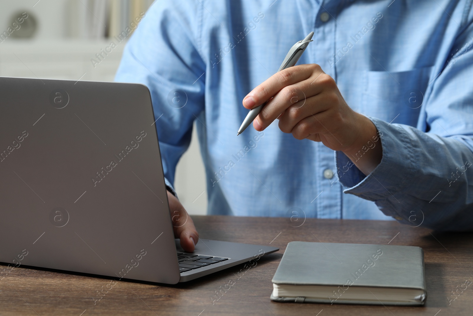 Photo of Man with pen and laptop at wooden table, closeup